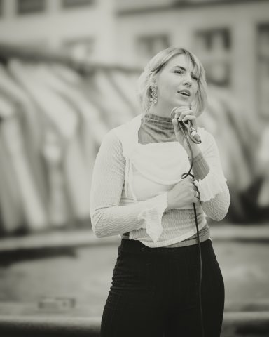 Frau mit Mikrofon, in der Nähe von farbigen Booten, lächelt selbstbewusst.